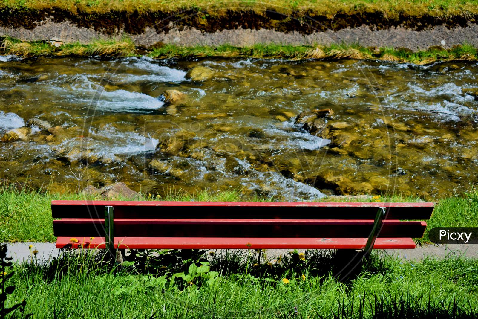 Empty red bench next to a small river in Switzerland 7.5.2020