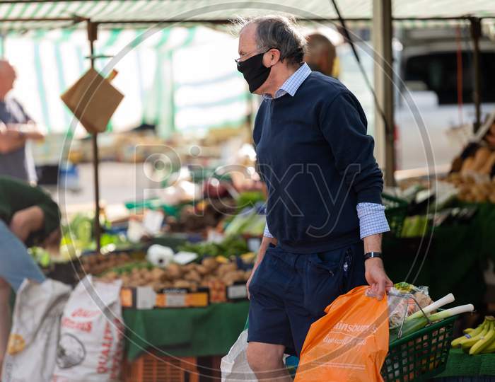 A Mature Man Wearing A Protective Face Mask Carries Shopping At An Outdoor Market