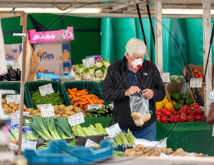 A Mature Man Wearing A Protective Face Mask Carries Shopping At An Outdoor Fruit And Veg Market Stall