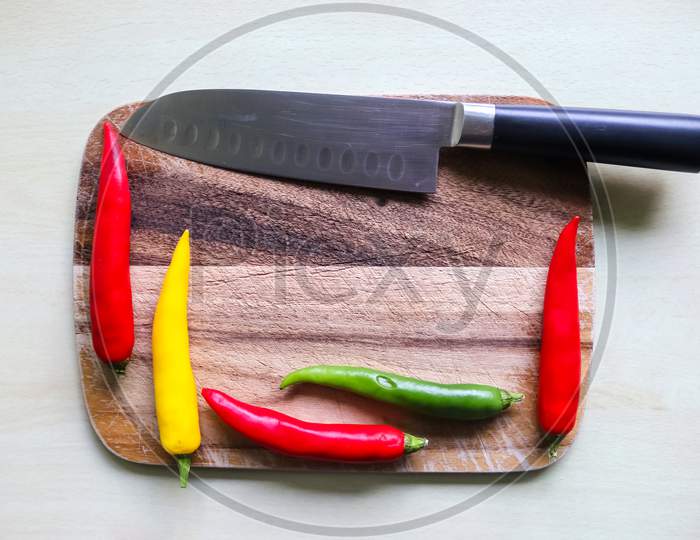 Top and perspective view of chili pepper and steel knife on a wooden cutting board with an isolated background