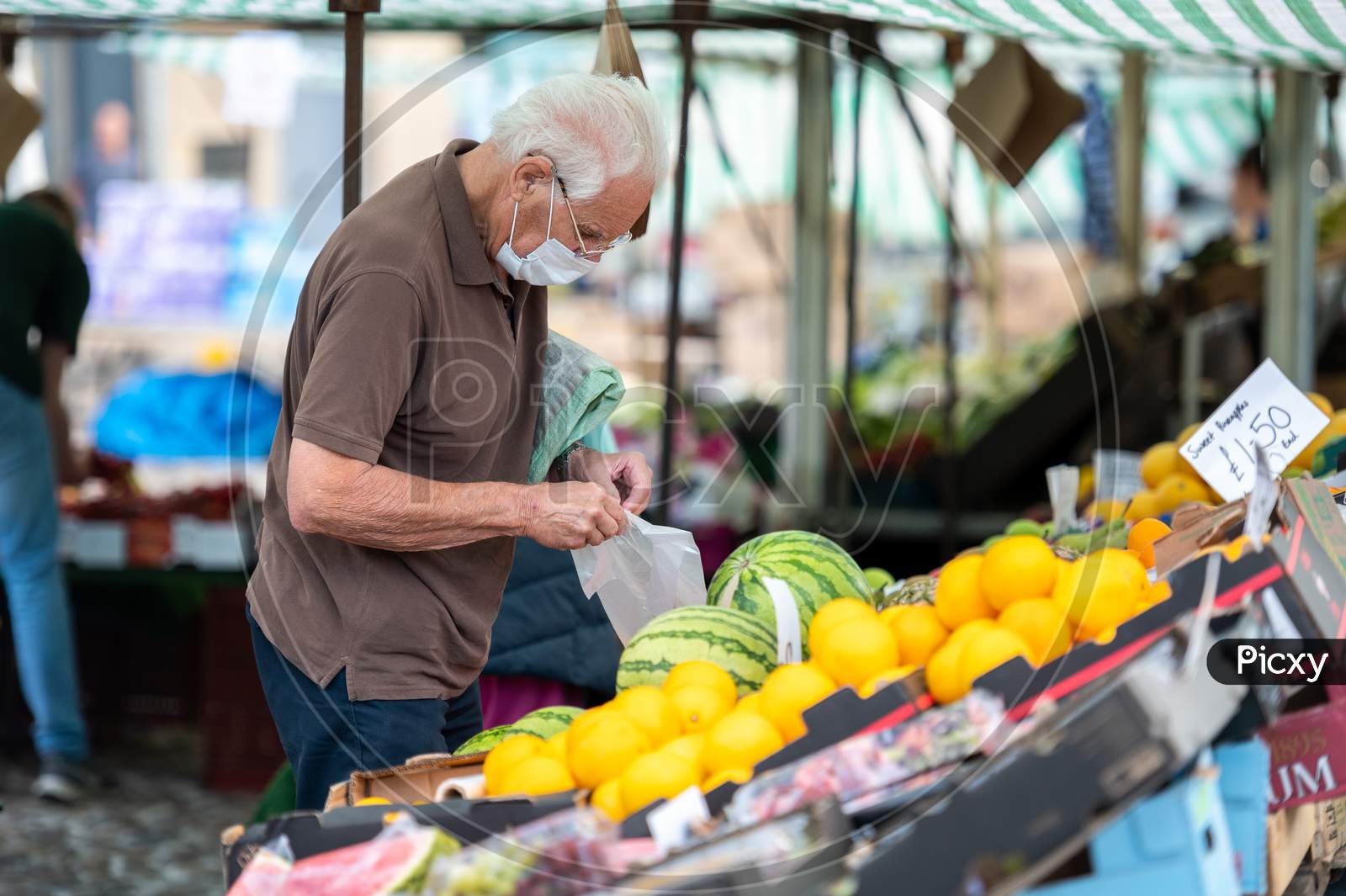 An Elderly Man Wearing A Protective Face Mask At An Outdoor Fruit And Veg Market Stall