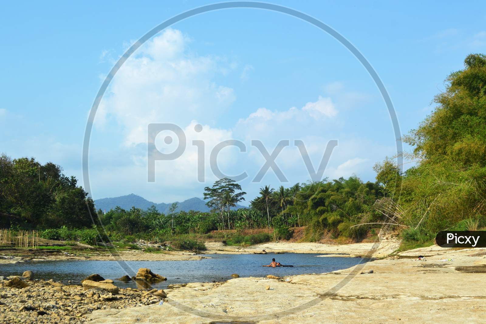 Beautiful View On A River With Little Water And Lots Rocks With Children Swimming And Beside The River Many Trees
