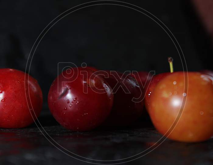 Closeup Of Fresh Red Juicy Plums With Droplets Of Water On A Black Background. Closeup Shot Of Satsuma Red Plums
