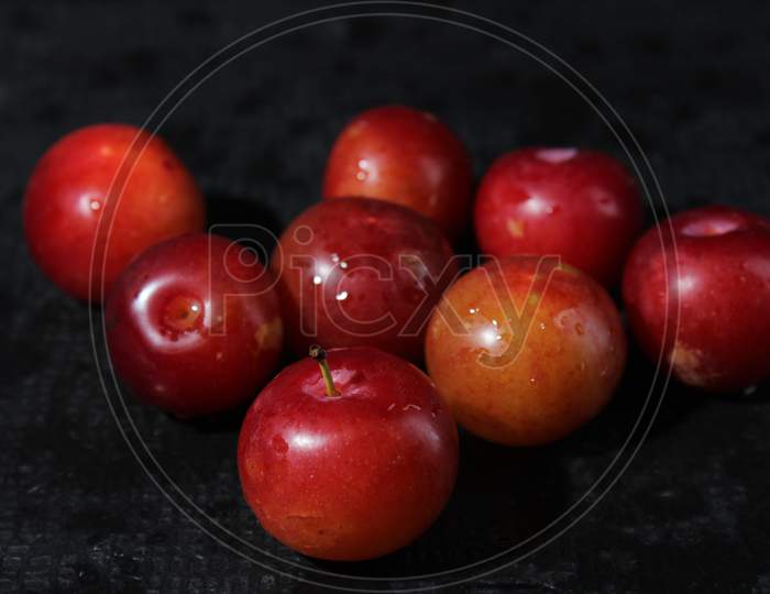Closeup Of Fresh Red Juicy Plums With Droplets Of Water On A Black Background. Closeup Shot Of Satsuma Red Plums