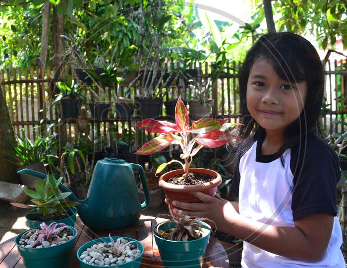 Smiling Beautiful Little Girl Sit While Holding A Potted Plant Looking At The Camera