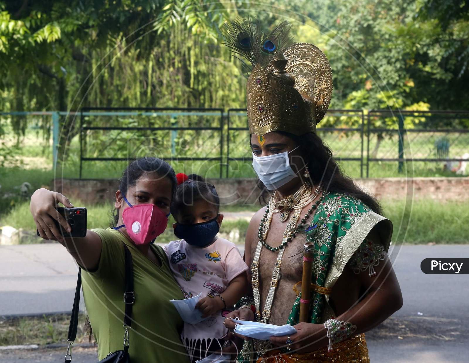 A woman takes selfie as a man dressed as Hindu Lord Krishna distributes masks to people at a road during Janmashtami celebrations, in Chandigarh August 11, 2020