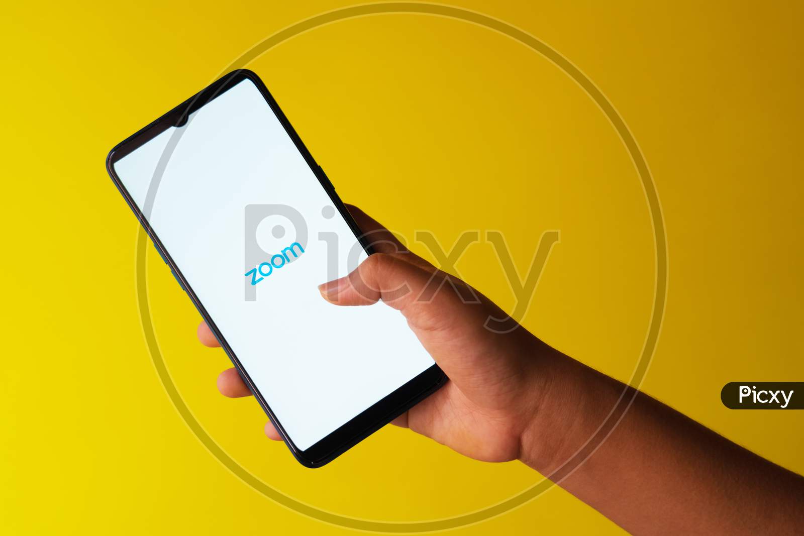 Zoom app logo on a smart phone held in hand against yellow extendable background with copy space