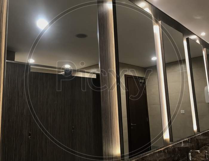 An Luxury Wash Room Or Rest Room Interiors Such As Beveled Type Mirror And Polished Marble Counter Top Wash Basin And Faucet Setup For An Male Toilet Area Of An Shopping Mall Or An Five Star Hotel