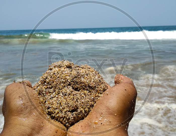 Hands holding a ball of sand facing towards the sea in India