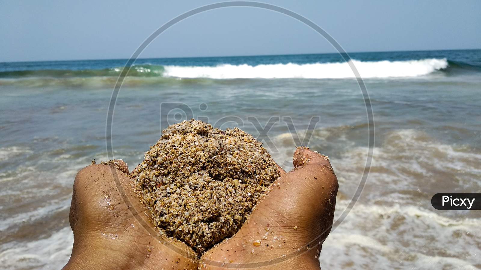 Hands holding a ball of sand facing towards the sea in India