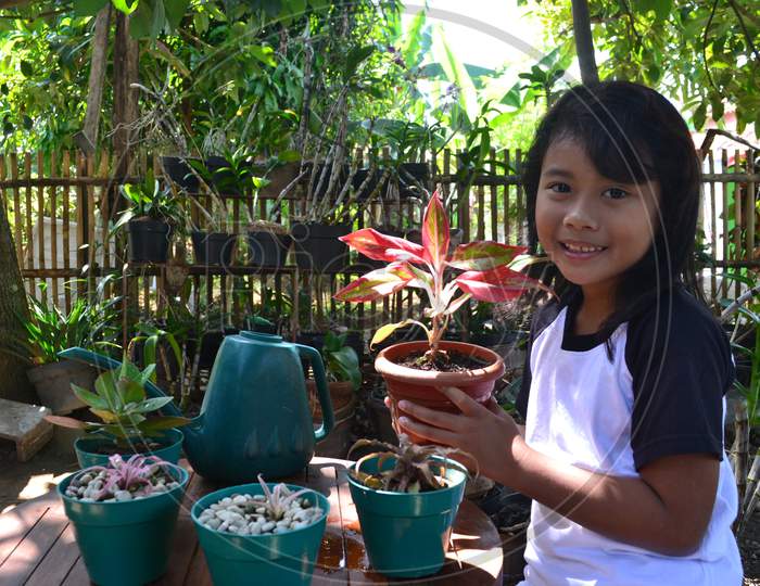 Toothy Asian Little Girl Sit While Holding A Potted Decorative Plant