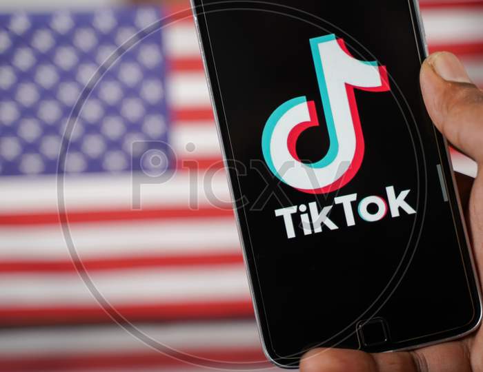 Maski, India - 4 August, 2020 : Close Up Of Hands Using Tik Tok App With Us Or American Flag As Background And Copy Space.
