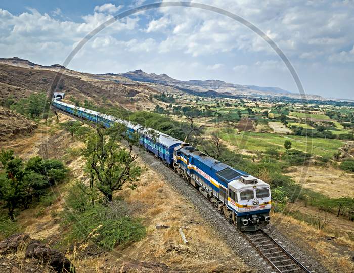 Shindawane, Pune, India:January 16Th, 2016-A Long Train Exits A Tunnel On A Clear Background Of Blue Sky With Clouds.