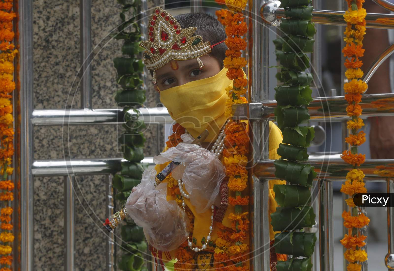 A boy wears mask and gloves, dressed as Hindu Lord Krishna arrive at a temple  during Janmashtami celebrations, in Chandigarh August 11, 2020