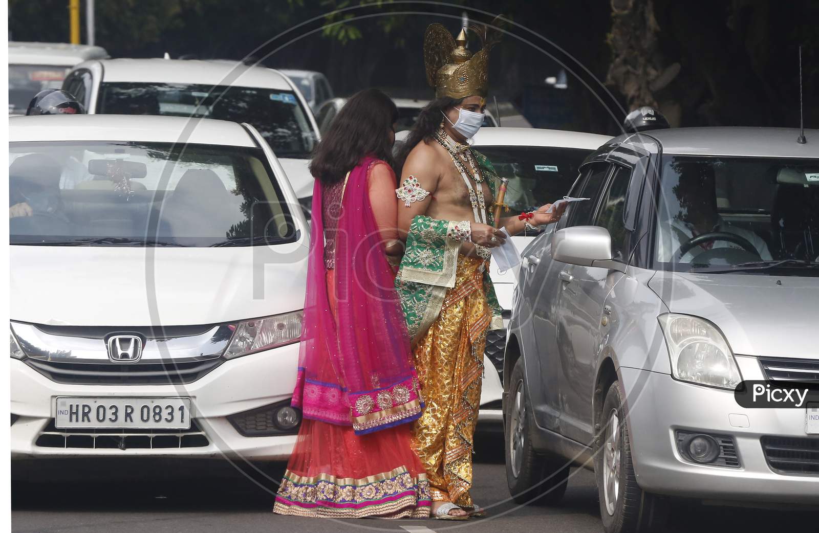A man wears mask  dressed as Hindu Lord Krishna and a woman dressed his consort Radha, distribute  masks to people at a road during Janmashtami celebrations, in Chandigarh August 11, 2020