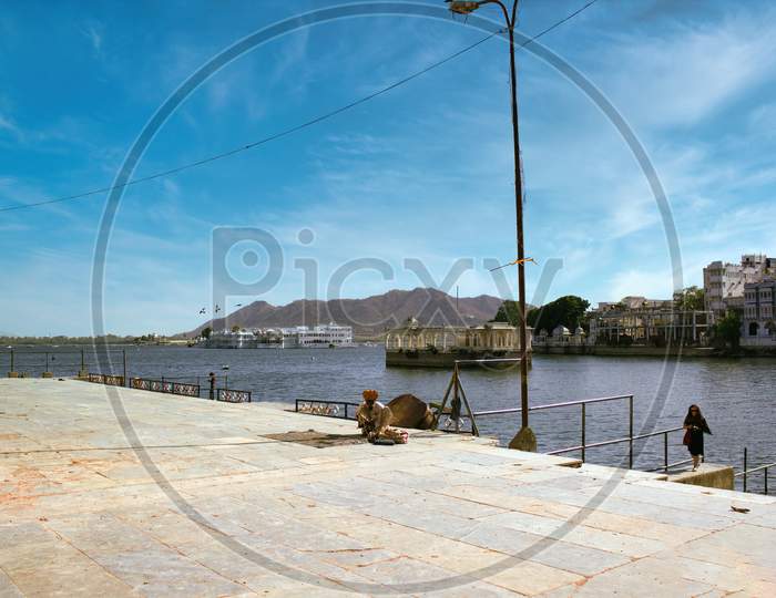 Udaipur, India - May 22, 2013: A Rajasthani Man In Indian Traditional Clothes Sitting Next To Lake Pichola Behind Bagore Ki Haveli Which Is Is One Of The Oldest Havelis