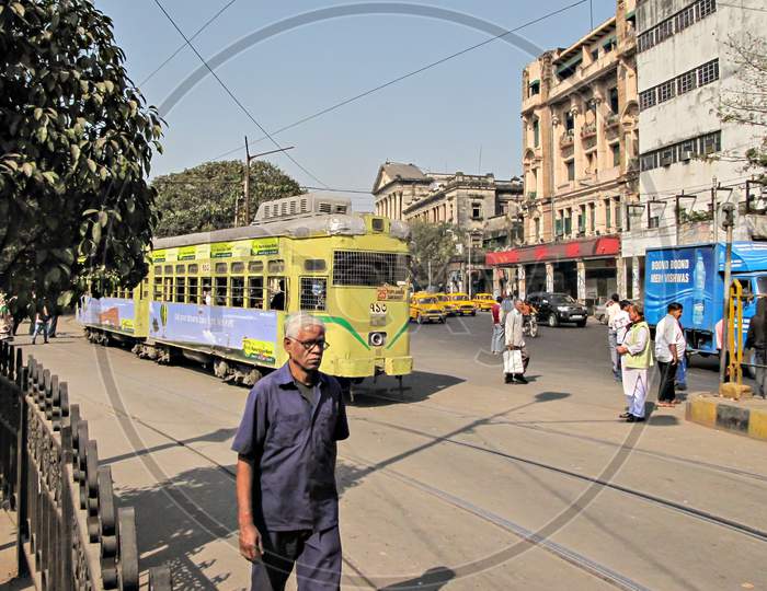 Kolkata, West Bengal, India-February 6Th,2012: Old Man Walks Along With Colorful Tram Exits Its Depot To Travel Through Busy,Crowded Streets Of Kolkata.