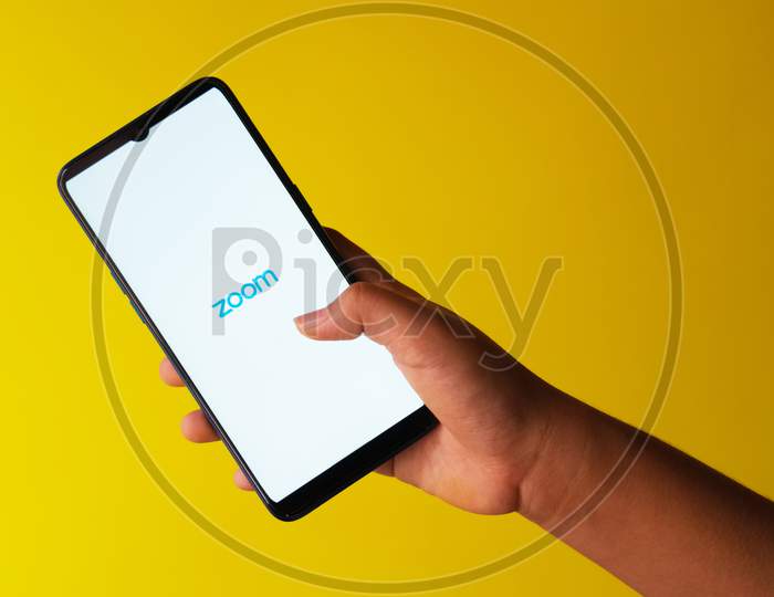 Zoom app logo on a smart phone held in hand against yellow extendable background with copy space