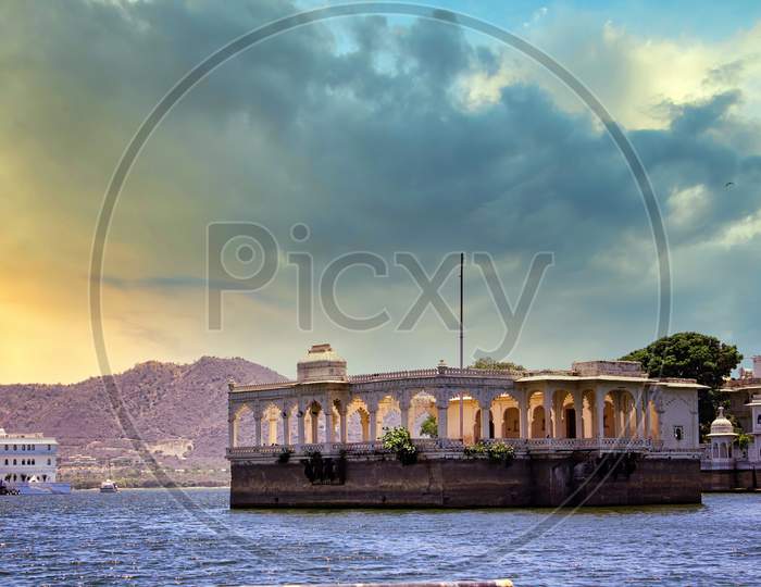Udaipur, India - May 25, 2013: Architecture Built Within Lake Pichola Surrounded By Hills Against Dramatic Clouds In Sunset