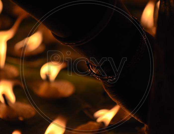 Creative Photography Of Many Realistic Burning Oil Lamps And Candles In A Festival In Evening. A Hand Is Lighting Colorful Red, Yellow, Fire Flame At Night On Dark Background With Noise, Grain Effect.