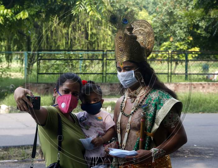 A woman takes selfie as a man dressed as Hindu Lord Krishna distributes masks to people at a road during Janmashtami celebrations, in Chandigarh August 11, 2020