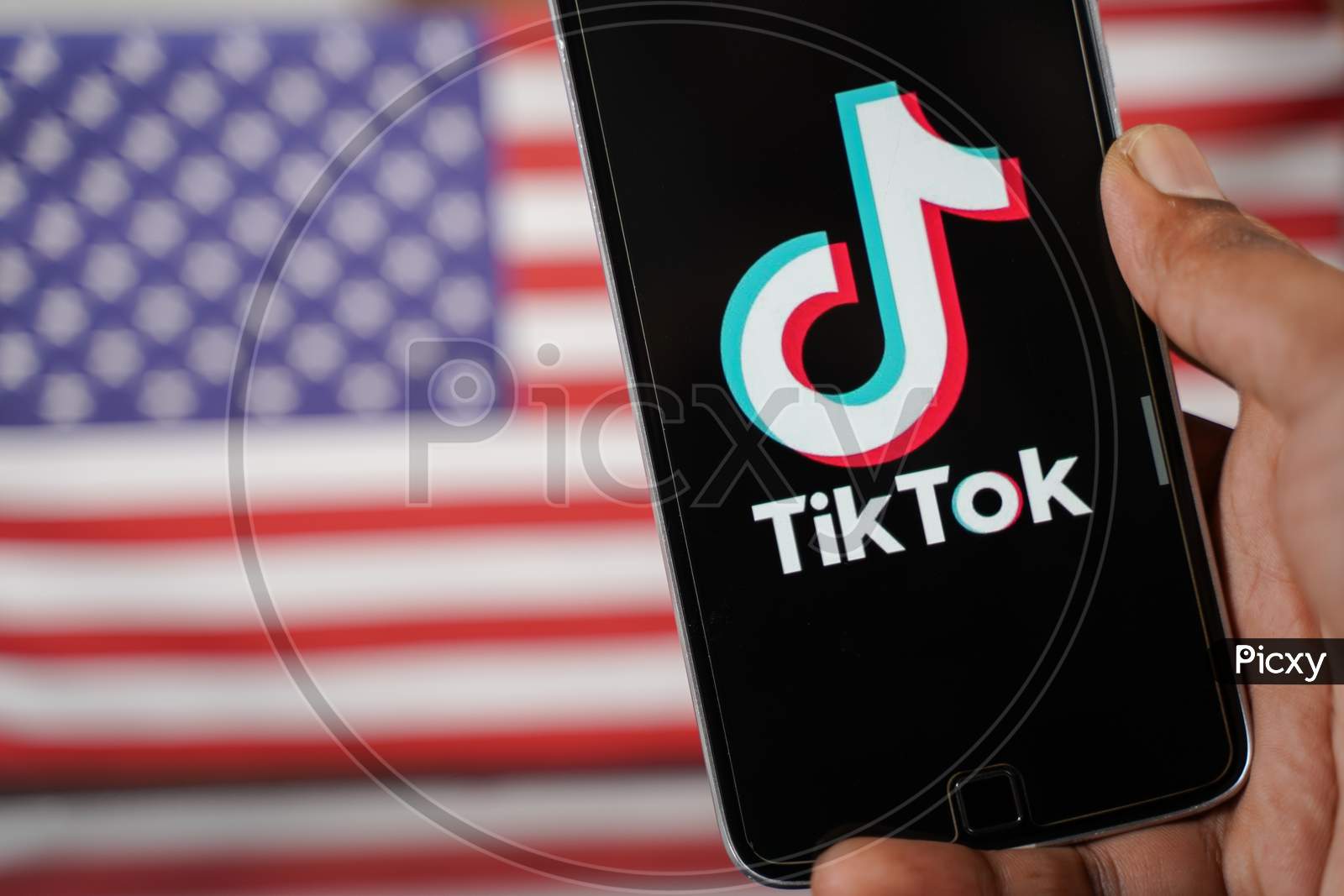 Maski, India - 4 August, 2020 : Close Up Of Hands Using Tik Tok App With Us Or American Flag As Background And Copy Space.