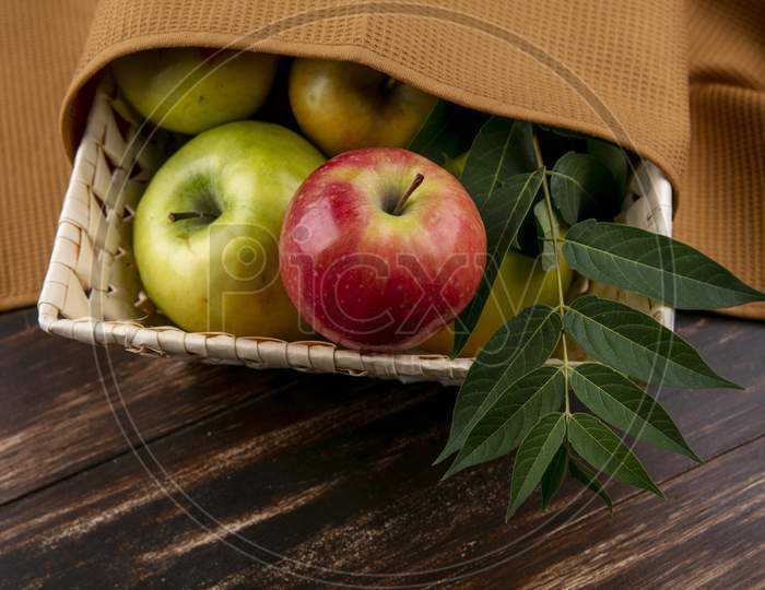 Side View Green And Red Apples In A Basket With A Branch And A Brown Towel On A Wooden Background