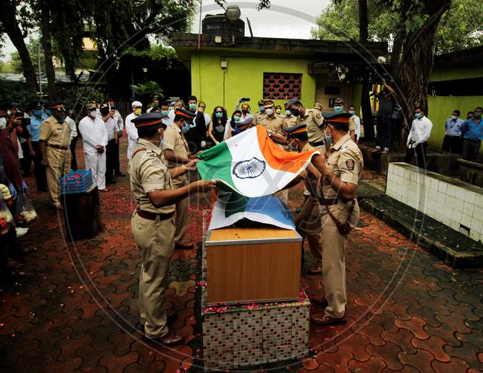 Police personnel lift the tricolor flag from the coffin of deceased Air India pilot Deepak Sathe as family members look on during his funeral in Mumbai, India on August 11, 2020.