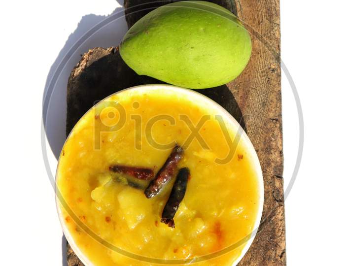 Mango Chutney In A Plate With A Raw Mango On Wooden Piece With White Background