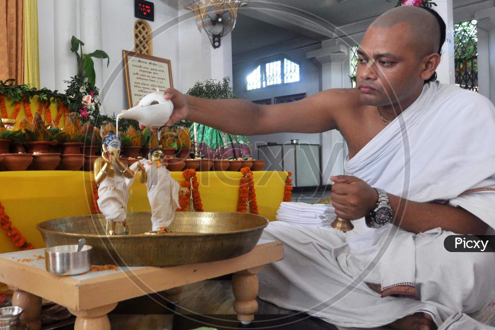 A saint performs 'Abhishek' On Idols Of Lord Krishna And Radha During Janmashtami In Guwahati On August 12,2020.