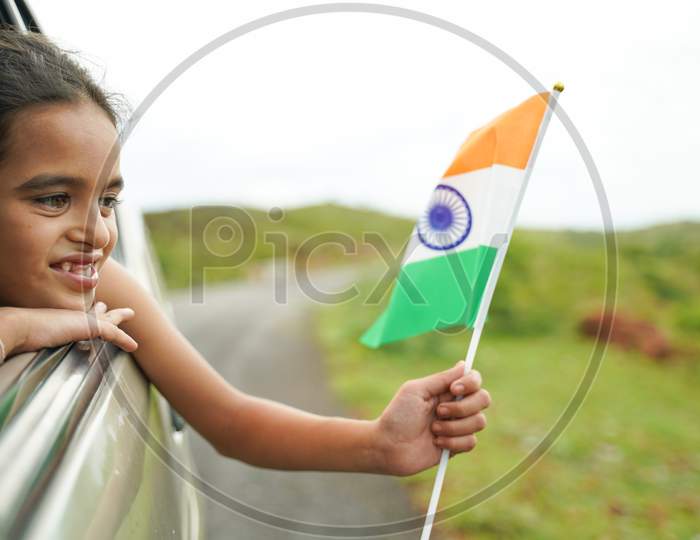 Happy Cheerful Young Girl Kid Holding Indian Flag Out Of In Moving Car Window - Concept Of Patriotism And Independence Or Republic Day Celebration
