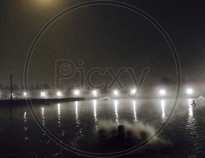 A row of lights with Moon reflecting in aquaculture pond water and with areators at night time