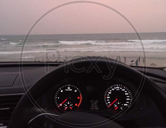 A view seeing at beach sitting inside a car with a view of speedometer dashboard and steering of Audi