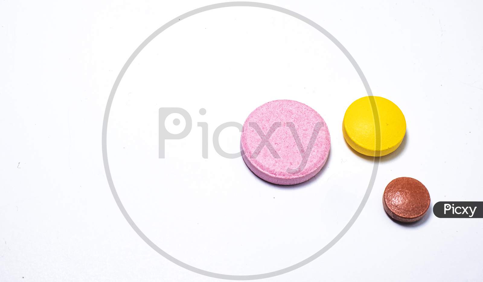 One White One Yellow And One Brown Pill On White Background.