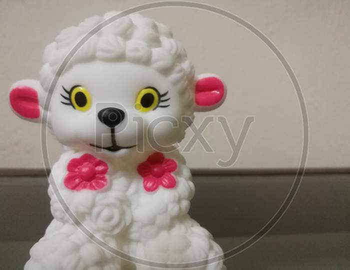 Closeup Shot Of A Sheep Doll With White Color And Red Color Ears And Flowers On It.