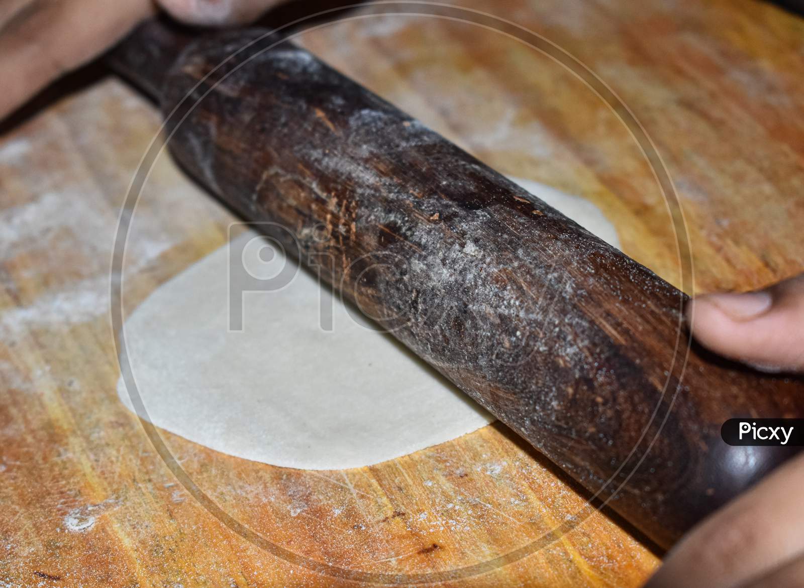 Close-up shot of a chakla belan (rolling board and pin) having shallow depth of field rolling over the roti of refined flour.