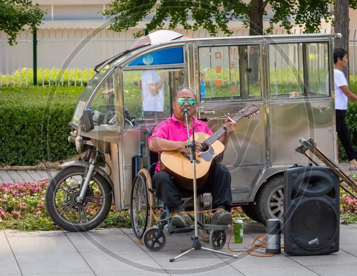 A Person With A Disability In A Wheelchair Playing Acoustic Guitar In The Street