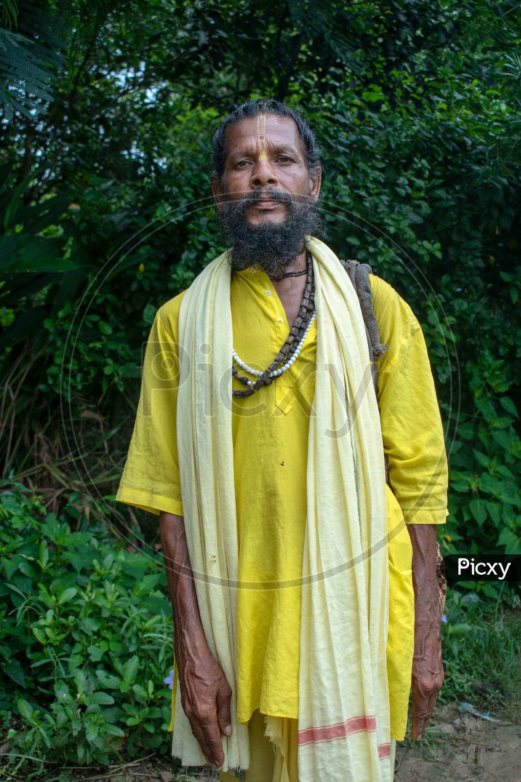 An Indian wanderer monk in a traditional yellow dress stands in a special posture.