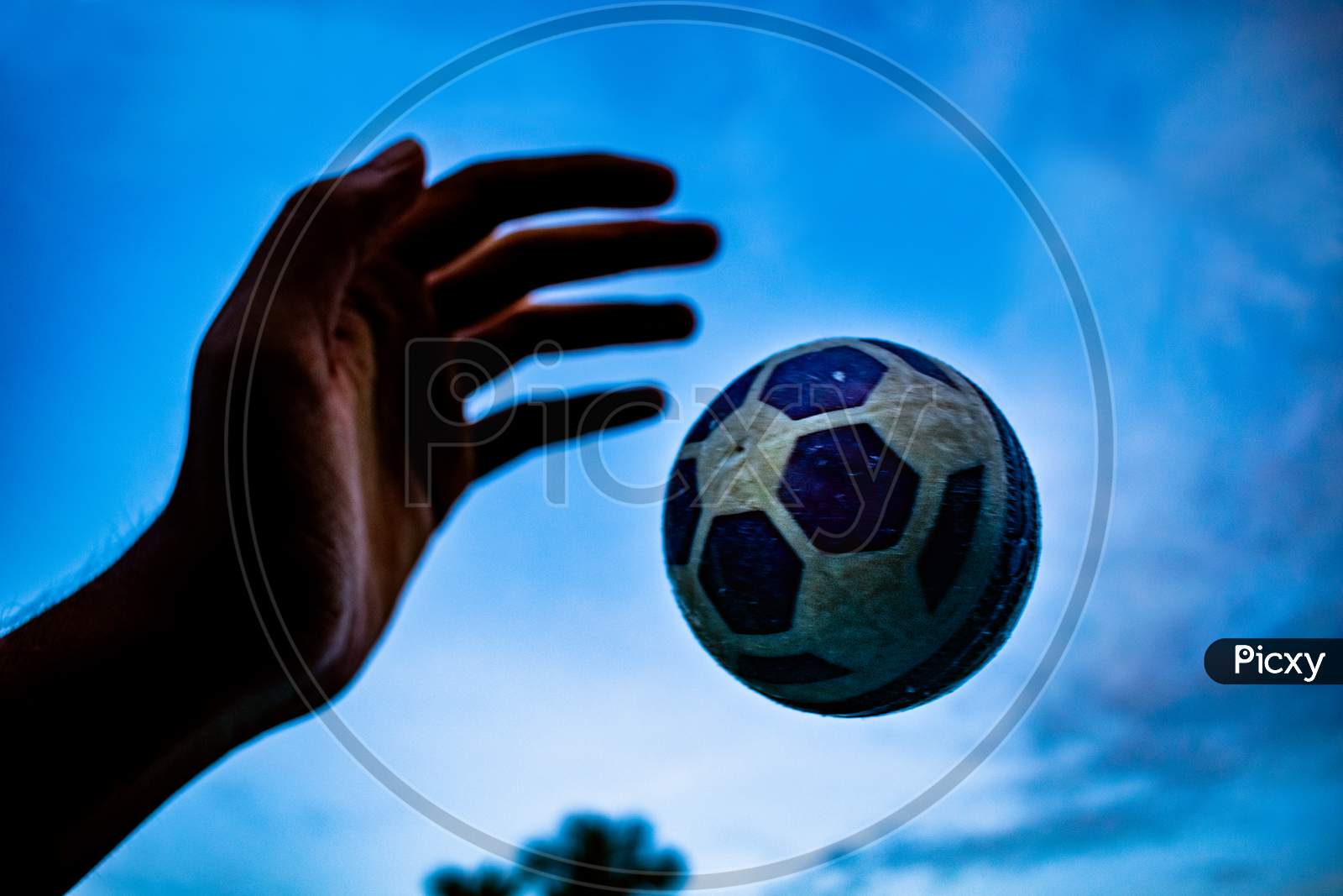 A Man Throwing Ball By Hand Against The Clear Blue Sky With White Clouds. Close up macro shot of plastic cricket ball float in air on blur nature background. Creative Photography, Copy Space For Text.