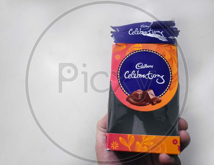 Hand holding a pack of Cadbury chocolates on a white background.