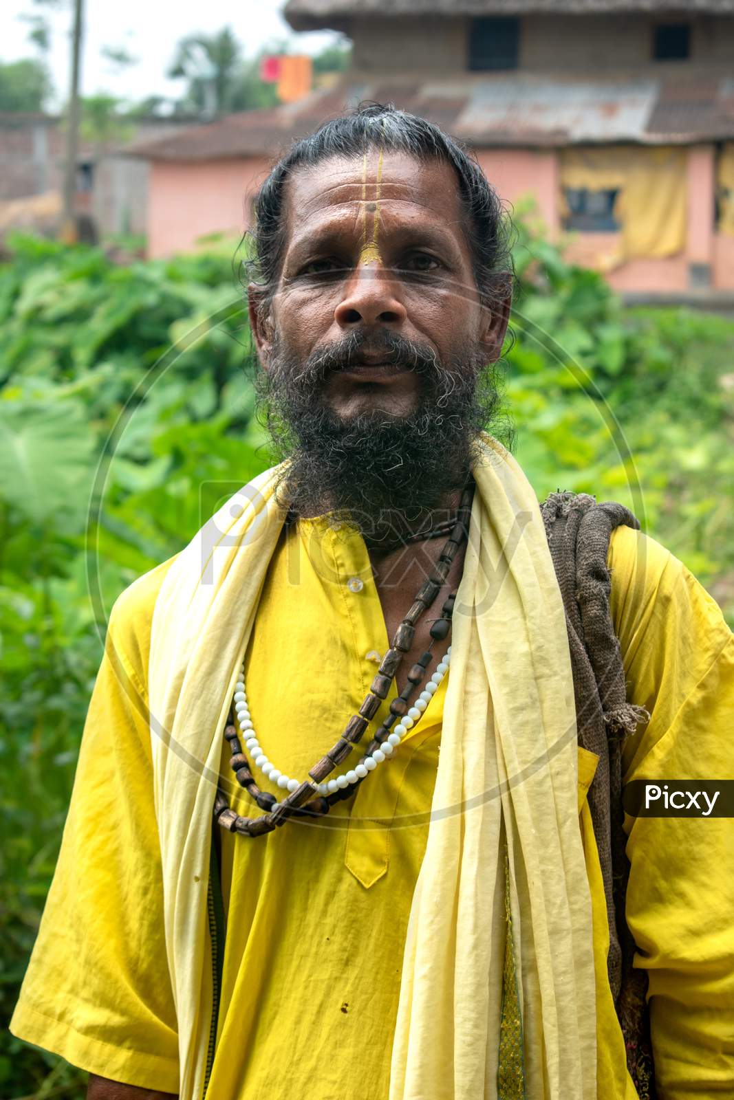 An Indian wanderer monk in a traditional yellow dress stands in a special posture.