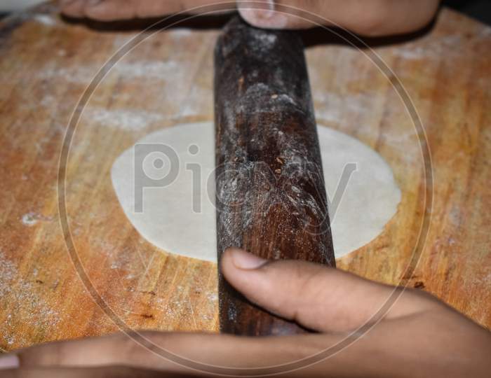 Close-up shot of a chakla belan (rolling board and pin) having shallow depth of field rolling over the roti of refined flour.