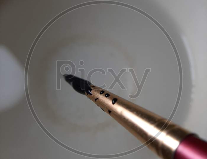 A photo of paint brush dipped in the black poster colour with its drops .