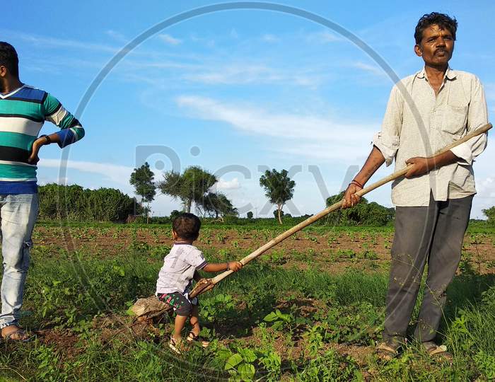 A young Indian child is having fun on a farm with his grandfather and uncle