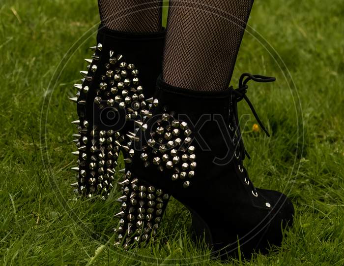 Rear Side View Of Pair Of Black Spiky Heels Suede Ankle Boots On Anonymous Fishnet Legs