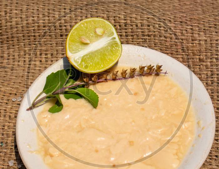 Indian Traditional Dahi (Curd) Or Yogurt In Plate With Lemon Slice And Basil Leaves  Isolated On Burlap Fabric Background In Vertical Orientation
