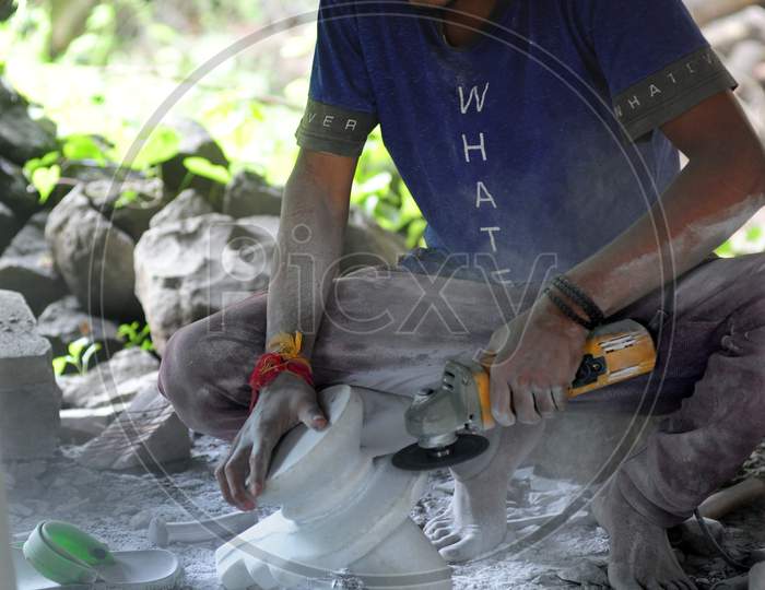 Young man working on a stone sculpture with a hand held motor grinder.