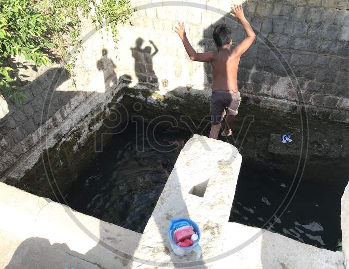 A Boy Jumping In Joy Into The Water Well In An Village Of An India