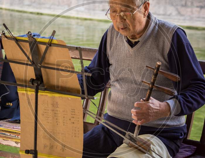 Elderly Man Playing Traditional Chinese Instrument At A Park In Beijing, China