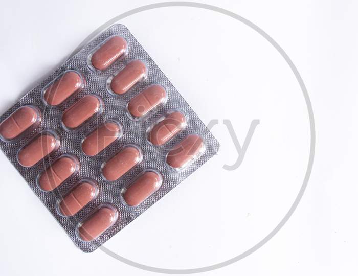 Brown Coloured Pills In Plastic Packaging On White Background.